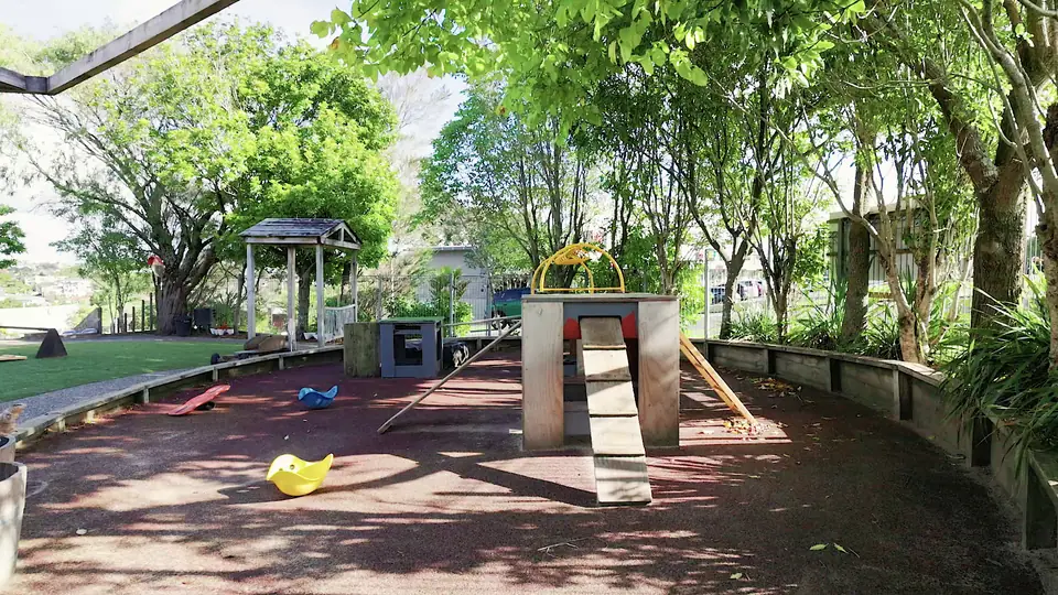 A bark playground under mature trees, with a wooden climber and a plank ramp.