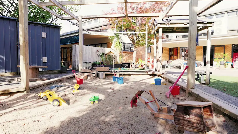 The sandpit under a pergola, with toy diggers and buckets.