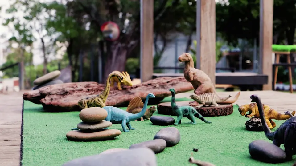 Toy dinosaurs on driftwood and stacked stones, on a patch of turf.