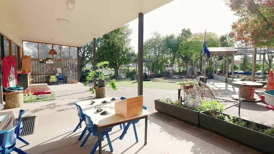 The covered deck, with small tables and chairs, planter boxes and the playground beyond.