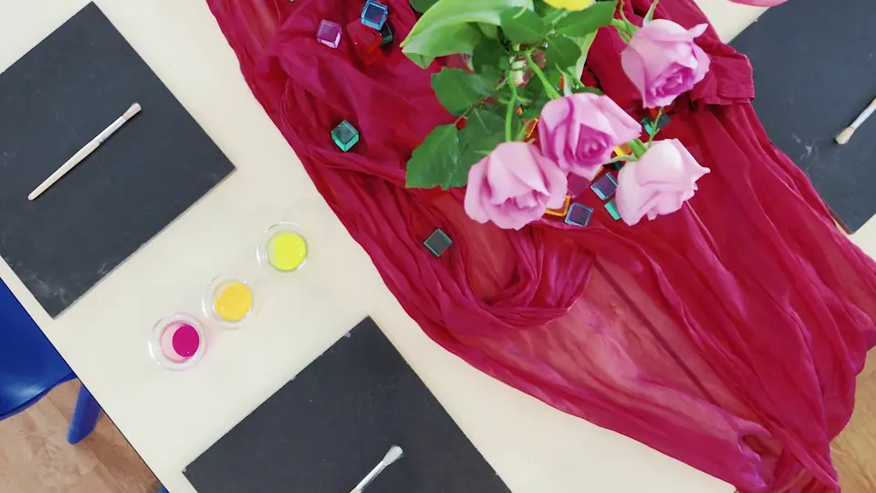 From above: slates, pots of coloured paint, and red silk with pink roses.