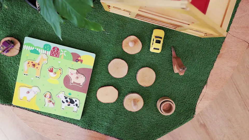 From above: a wooden farm-animal puzzle and tree cookies on a square of turf.