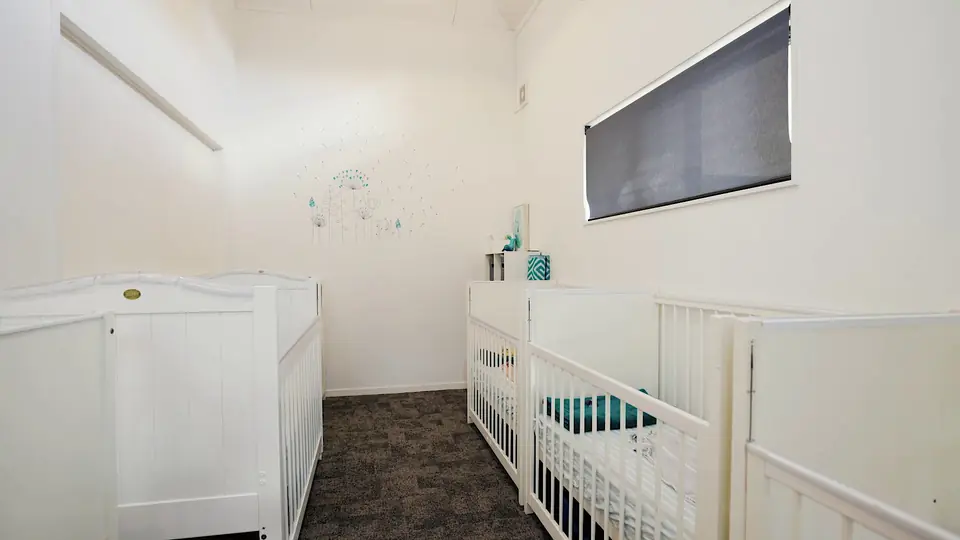 White cots in a sleep room, under a window with a blind.