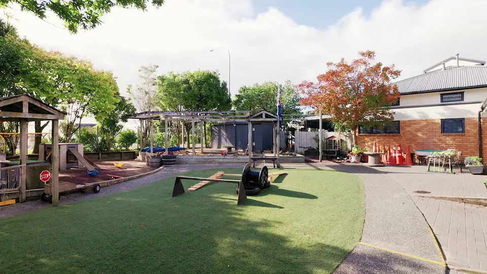 The playground lawn, with a balance beam, a cable drum and pergolas along its edge.