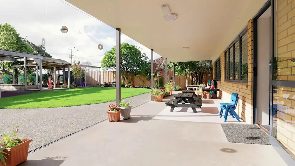 The covered deck along the brick building, with picnic tables and potted flowers.