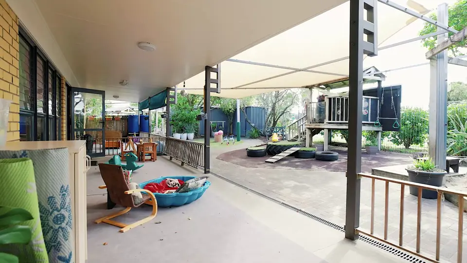 A paddling pool full of cushions on the covered deck, beside a bentwood chair.