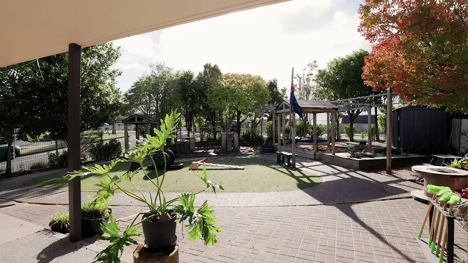 The paved yard, with a potted plant in front and pergolas under the trees behind.