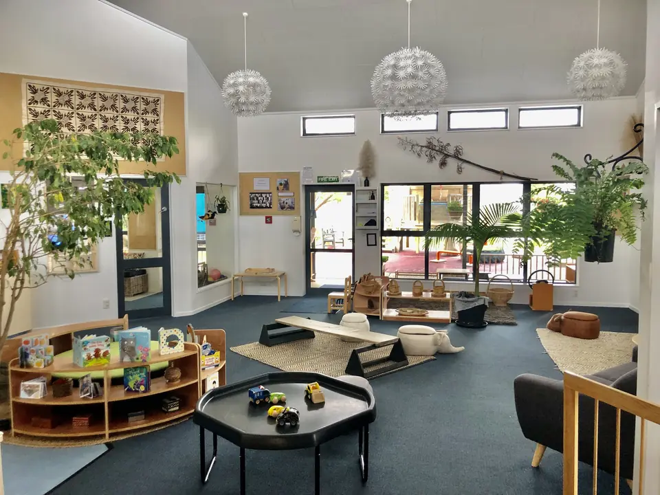 A room with paper lanterns hanging from a high ceiling, a round rug, a black table of toy vehicles and low wooden shelves of books.