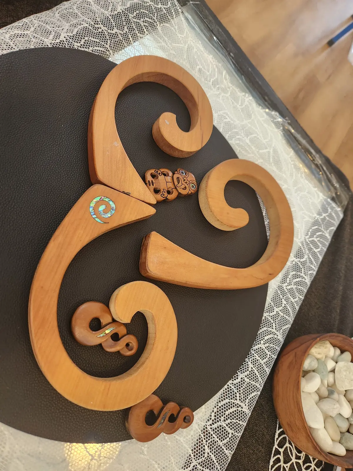 A wooden koru shape with small pounamu-style pieces on a dark mat.