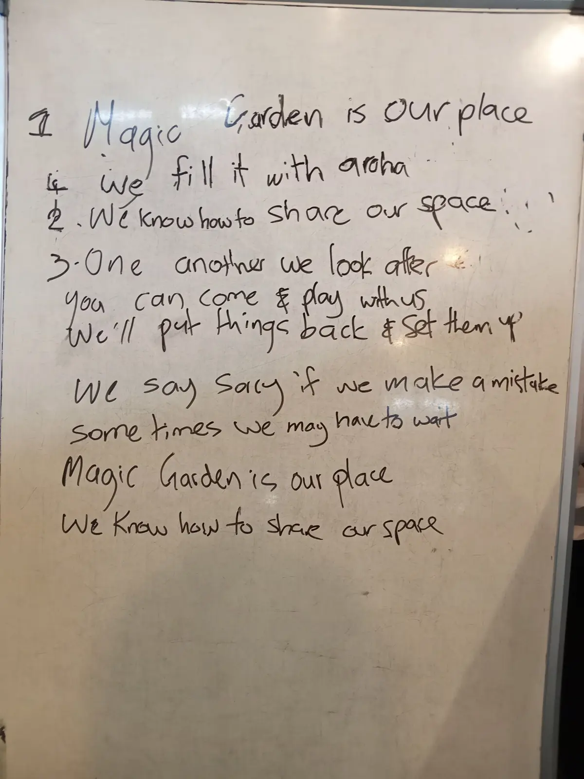 The room's song written by hand on a whiteboard, starting: Magic Garden is our place, we fill it with aroha.