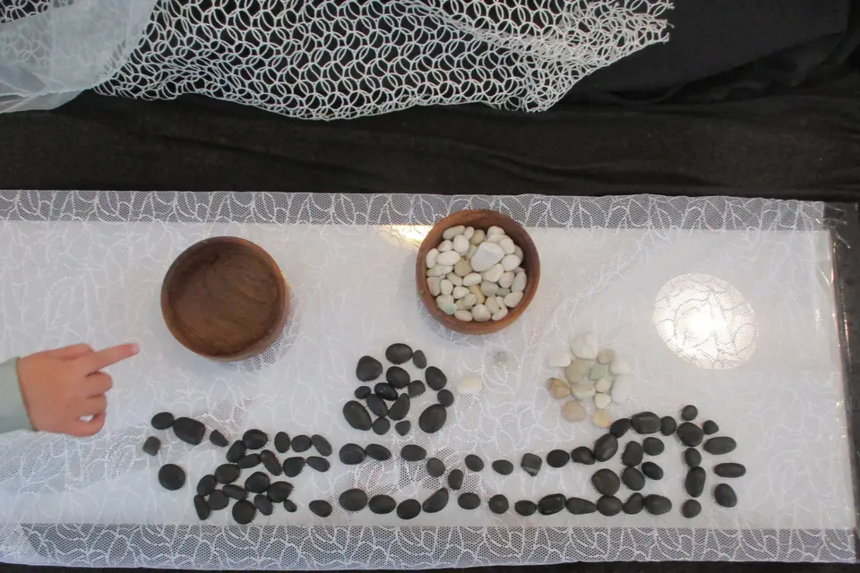 A child's finger pointing at a pattern of black stones laid on lace.