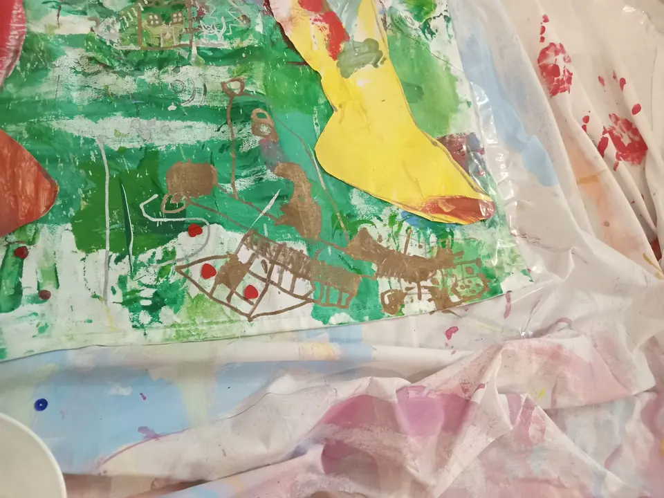 A group painting in greens, yellows and reds on a drop sheet.