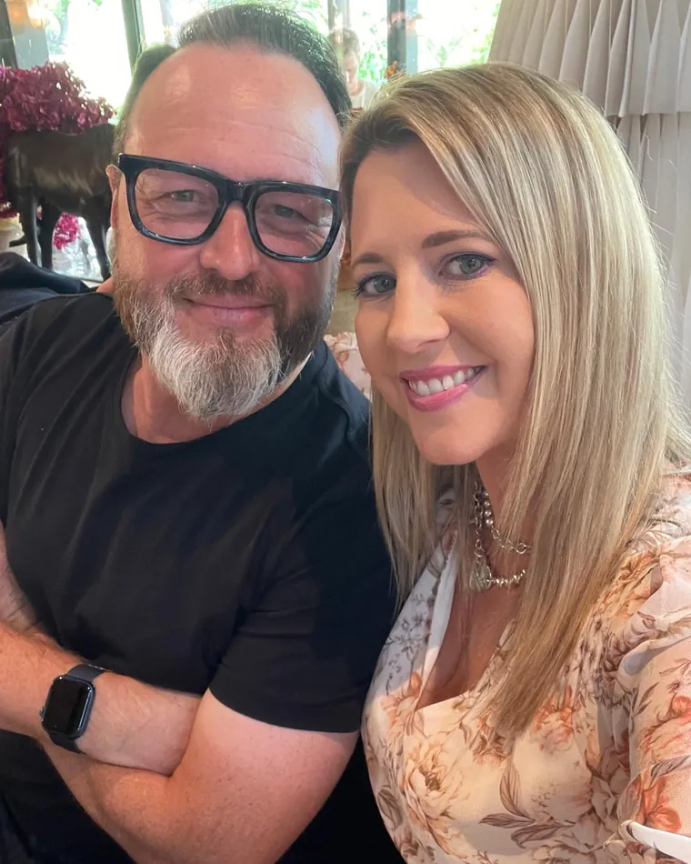 Andrew and Gemma, side by side and smiling, at a table by a window.