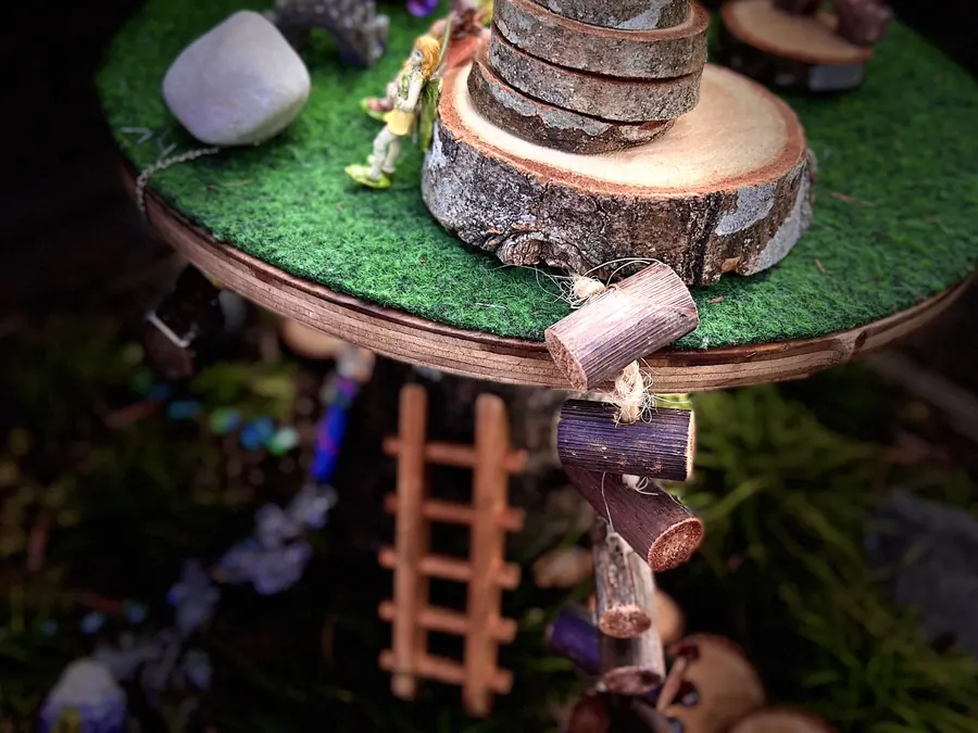 A fairy garden laid out on a round felt-topped table, with small houses, moss and stones, against a dark background.