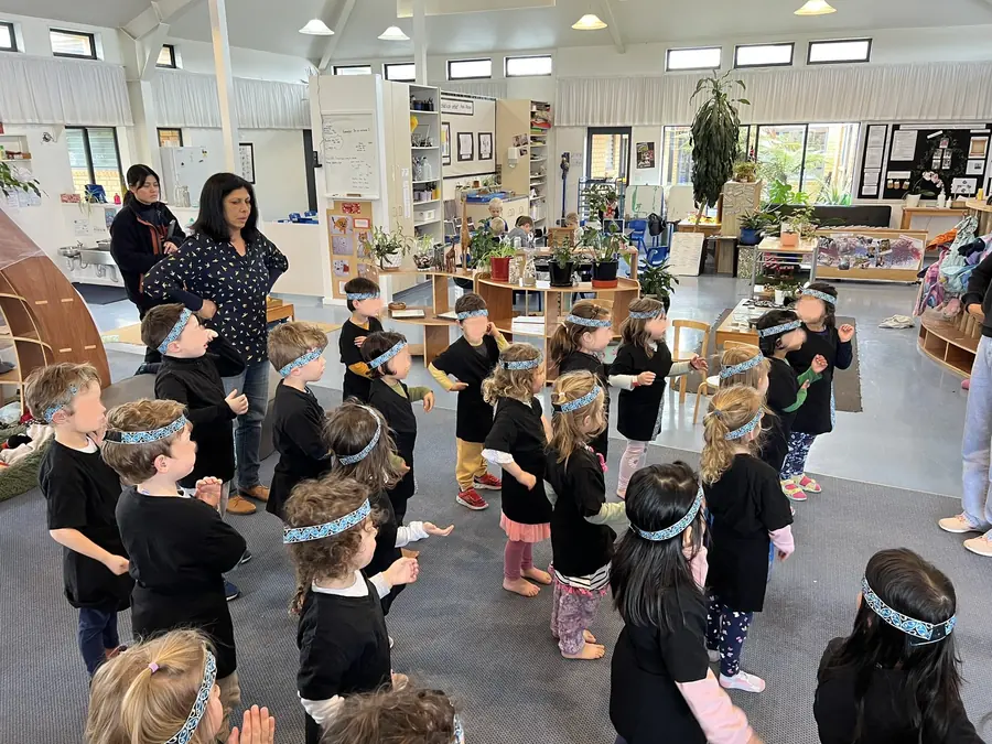 The kapa haka group in the hall at Northcross: children in black with patterned headbands stand in rows, arms raised, with their teachers watching.